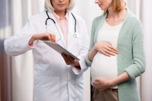 doctor showing results of examination to young pregnant woman on digital tablet